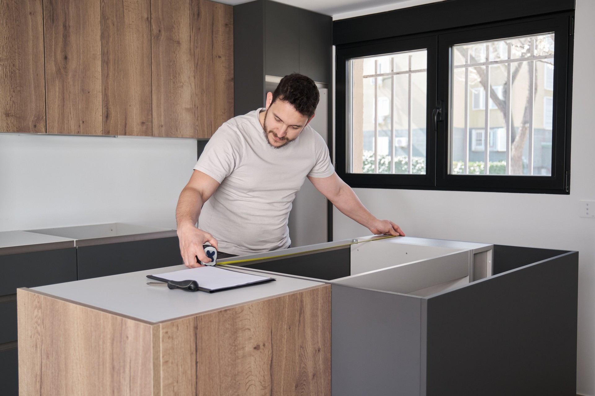 Young hispanic man using measuring tape before placing countertops on kitchen.